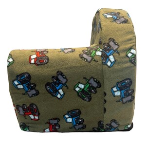 Puede incluir: Un sill&oacute;n de peluche verde con un patr&oacute;n de tractor. El sill&oacute;n tiene forma de sill&oacute;n grande con respaldo y brazos. La tela es suave y peluda.