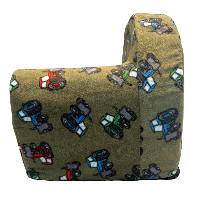 Puede incluir: Un sill&oacute;n de peluche verde con un patr&oacute;n de tractor. El sill&oacute;n tiene forma de sill&oacute;n grande con respaldo y brazos. La tela es suave y peluda.