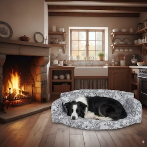 Puede incluir: Un perro Border Collie blanco y negro descansando sobre una cama para perros estampada en una cocina. La cama para perros tiene un patrón gris y blanco. Una chimenea con fuego ardiendo está en el fondo.