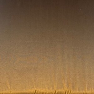 May include: A close-up of a gold fabric with a subtle sheen. The fabric has a smooth texture and a slightly wrinkled appearance.