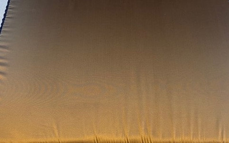 May include: A close-up of a gold fabric with a subtle sheen. The fabric has a smooth texture and a slightly wrinkled appearance.