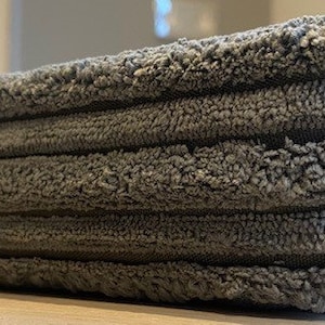 May include: A close-up of a gray, textured, rectangular bath mat with a ribbed design.