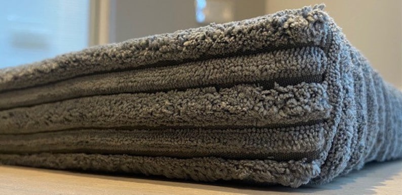May include: A close-up of a gray, textured, rectangular bath mat with a ribbed design.