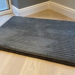May include: A gray corduroy dog bed with a rectangular shape. The bed is lying on a light wood floor.