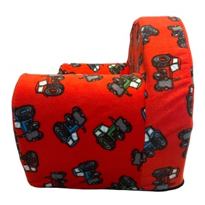 Puede incluir: Sill&oacute;n rojo para ni&ntilde;os con estampado de tractor. El sill&oacute;n est&aacute; hecho de tela suave y tiene un respaldo y brazos redondeados.