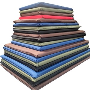 May include: A stack of rectangular cushions in various colors, including blue, brown, black, and green. The cushions are neatly arranged, creating a layered effect. The image is set against a plain white background.