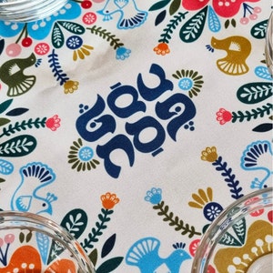 May include: A white fabric with a blue floral pattern and the Hebrew words "Shabbat Shalom" in blue lettering.