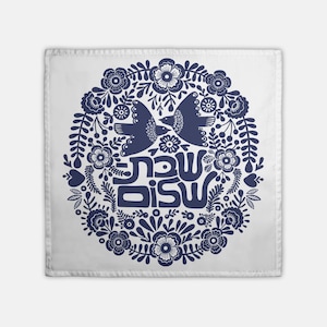 May include: A white square dish towel with a blue floral design. The design features two birds facing each other, a circle of flowers, and the Hebrew words "Shanah Tovah" in the center.