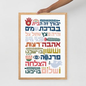 May include: A framed print with a white background and colorful Hebrew text. The text is arranged in a vertical column and includes words like "blessing", "love", and "peace". The print is decorated with various illustrations, including a hand, a rainbow, a heart, a flower, a dove, and an eye.