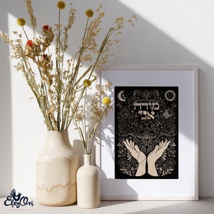 May include: A black and gold print with the Hebrew words "Todah Rabah" meaning "I give thanks" in a decorative floral design with hands raised in prayer. The print is framed in a white frame and is displayed on a table with dried flowers in a vase.