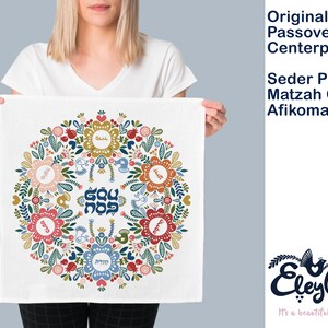 May include: A white fabric Passover Seder plate cover with a colorful floral design and Hebrew text. The design features a circle of flowers with a central star and the words "Dayenu" and "Ma Nishtana" in Hebrew.