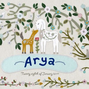 May include: A white and brown felt applique of a horse and foal standing under a green and white felt tree with flowers. The name "Arya" is written in blue felt below the animals. The date "Twenty eighth of January 2011" is written in black felt below the name.