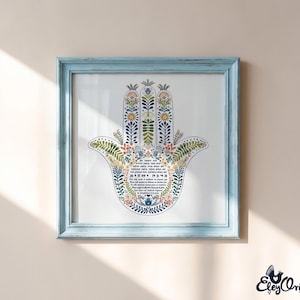 K&ouml;nnte beinhalten: Ein gerahmter Druck mit einem Hamsa-Hand-Design, verziert mit farbenfrohen Blumenmustern in Blau, Gr&uuml;n und Gelb. Der Druck ist in einem hellblauen Holzrahmen eingefasst. Text ist sichtbar.