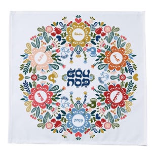 May include: White fabric with a colorful floral design featuring a circle of flowers with Hebrew text in the center. The text reads "Blessed are you, Lord our God, King of the Universe, who sanctifies us with His commandments and commands us to kindle the Sabbath lights."
