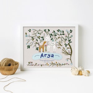 May include: A framed embroidery featuring a white unicorn and a brown fawn standing in a floral garden. The name "Arya" is embroidered in blue lettering below the animals. The text "Twenty eighth of January 2017" is also embroidered below the name.