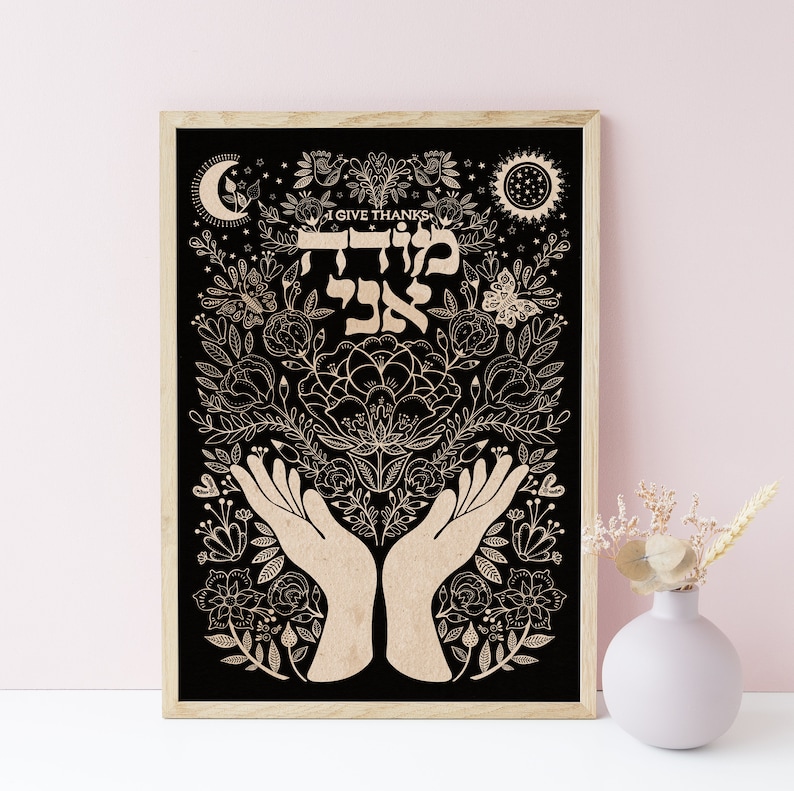 May include: A black and white print with a floral design and two hands cupped together. The text "I Give Thanks" and the Hebrew word "Modeh Ani" are written in the center of the print.