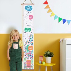 May include: A white height chart with a wooden top and bottom, featuring colorful floral and bee illustrations. The chart includes the phrases "bee mable", "bee you", "bee brave", and "bee kind", with a measurement scale in inches.