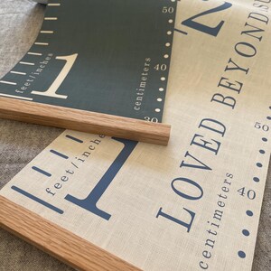 Two personalised canvas family growth charts with wooden frames. The chart on the left has a dark blue background with oak hangers. The family height chart on the right has a beige background with blue numbers and oak hangers.