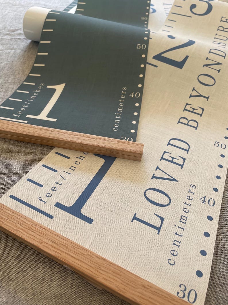 Two personalised canvas family growth charts with wooden frames. The chart on the left has a dark blue background with oak hangers. The family height chart on the right has a beige background with blue numbers and oak hangers.
