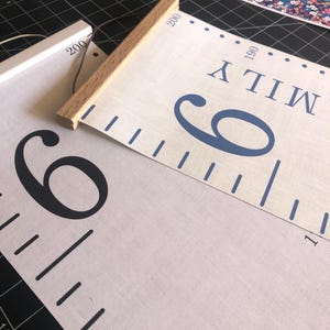 Charcoal numbers/ pale grey background height chart with white hangers next to Blue numbers/ biscuit background height chart with oak hangers