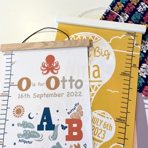 May include: Two children's growth charts with wooden and white hanging rods. One chart is white with an octopus, the name "Otto", and the date "16th September 2022". The other is yellow with the text "Big", "July 6th 2023", and height markings up to 62 inches.