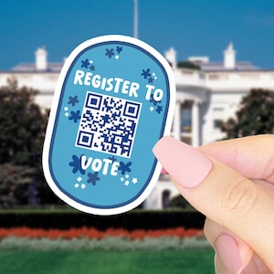 May include: A light blue sticker with the words "REGISTER TO VOTE" and a QR code. The sticker is decorated with white flowers and held in front of the White House.