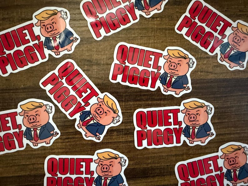 May include: A collection of stickers featuring a cartoon pig with blonde hair, wearing a suit and tie. The stickers have the text "QUIET, PIGGY" in red letters. The stickers are scattered on a wooden surface.