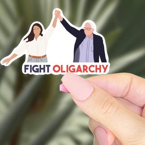 Puede incluir: Una pegatina blanca con una ilustración de dibujos animados de dos personas levantando los puños en el aire. El texto "FIGHT OLIGARCHY" está impreso en letras rojas y azules debajo de la ilustración.