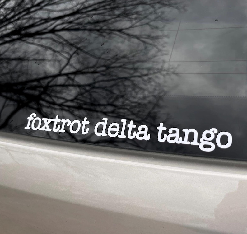 May include: A white vinyl sticker with the text "foxtrot delta tango" on a black car.