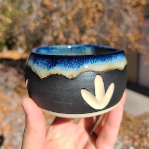 May include: A small black ceramic bowl with a blue and white glaze. The bowl has a white arrow design on the side.