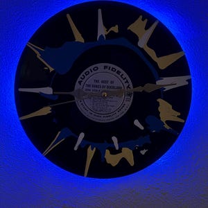 May include: A black vinyl record clock with a painted design in blue, yellow, and white. The clock face features the text "AUDIO FIDELITY" and "THE BEST OF THE DUKES OF DIXIELAND". The clock hands are gold-colored.