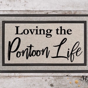 May include: Rectangular doormat with a grey border and the text "Loving the Pontoon Life" in black script. The background is a light beige colour, and the mat has a textured appearance. The doormat is designed for outdoor use.