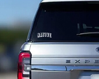 May include: A silver car with a black rear window and a white vinyl sticker that says "NATIVE" on the back.