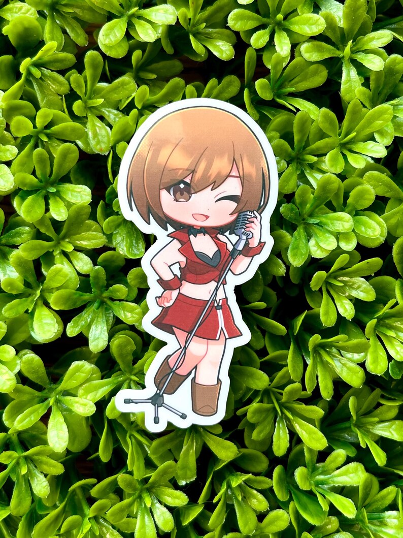 May include: A sticker featuring an anime-style character in a red outfit, holding a microphone. The character has brown hair and is winking. The sticker is set against a background of green foliage.