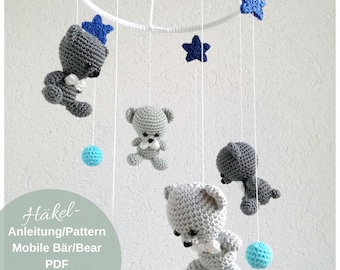 May include: A grey and blue crocheted baby mobile with four teddy bears and five stars hanging from a white ring. The mobile is made with soft yarn and is perfect for a nursery.