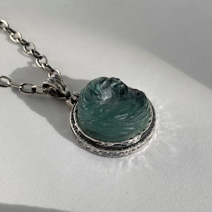 Puede incluir: Un collar de cadena de plata con un colgante que presenta una piedra verde tallada engastada en un bisel de plata.