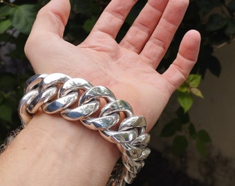 May include: A silver chain bracelet with large, chunky links. The bracelet is worn on a person's wrist.
