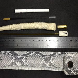 May include: A white bone pipe with a snake-like design, a gold metal rod, a white cigarette holder, a gold metal cap, and a black and white snakeskin carrying case.