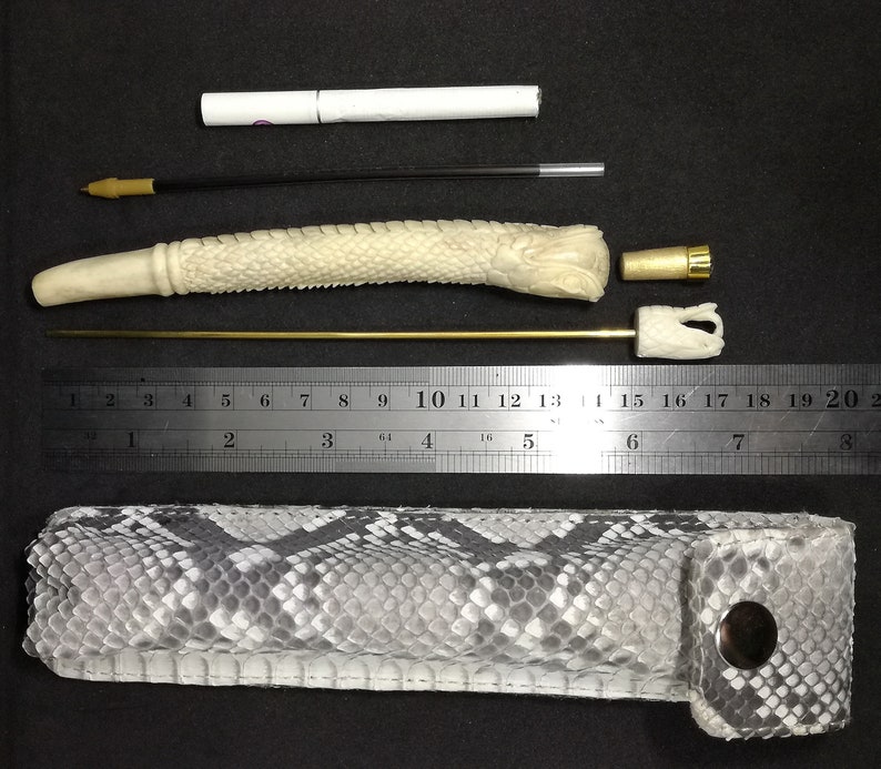 May include: A white bone pipe with a snake-like design, a gold metal rod, a white cigarette holder, a gold metal cap, and a black and white snakeskin carrying case.