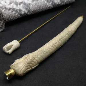 May include: A white bone pen with a snake design and a gold cap with a clear crystal. The pen comes with a separate gold metal rod.
