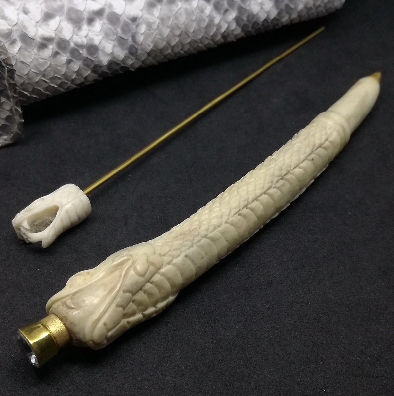 May include: A white bone pen with a snake design and a gold cap with a clear crystal. The pen comes with a separate gold metal rod.