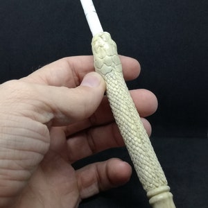 May include: A white, hand-carved, snake-shaped smoking pipe with a textured surface.