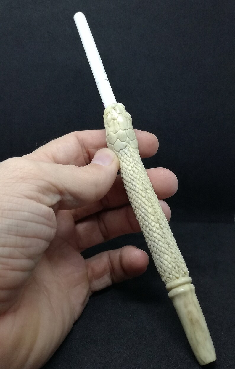 May include: A white, hand-carved, snake-shaped smoking pipe with a textured surface.