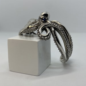 Peut inclure: Bracelet en argent en forme de pieuvre avec des pierres précieuses bleues pour les yeux. Le bracelet est fait d'un travail d'argent détaillé et a une finition texturée.
