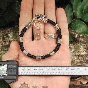 Puede incluir: Pulsera trenzada negra con cierre de cabeza de drag&oacute;n plateado y cuentas plateadas. La pulsera mide 14 cm de largo.