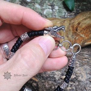 Puede incluir: Un brazalete trenzado negro con detalles de cabeza de drag&oacute;n plateados y un cierre plateado. El brazalete se muestra en la mu&ntilde;eca de una persona.