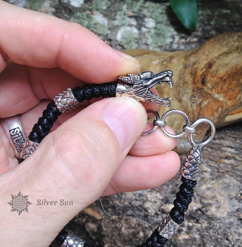 Puede incluir: Un brazalete trenzado negro con detalles de cabeza de drag&oacute;n plateados y un cierre plateado. El brazalete se muestra en la mu&ntilde;eca de una persona.