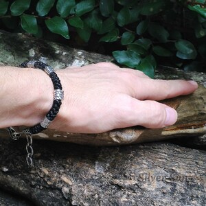 Puede incluir: Un brazalete de cuero negro con detalles plateados. El brazalete tiene un dise&ntilde;o trenzado y un cierre de broche.