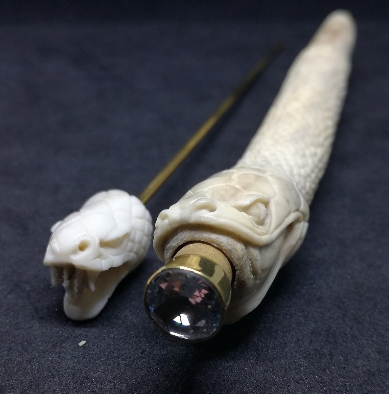 May include: Two intricately carved bone snake head walking sticks with a crystal at the end of one. The snake heads are detailed with scales and fangs.