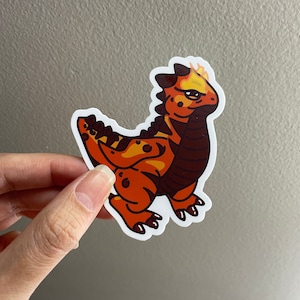 May include: A sticker of a cartoon orange and brown dragon with yellow flames on its head. The dragon has a black and brown striped neck and tail.